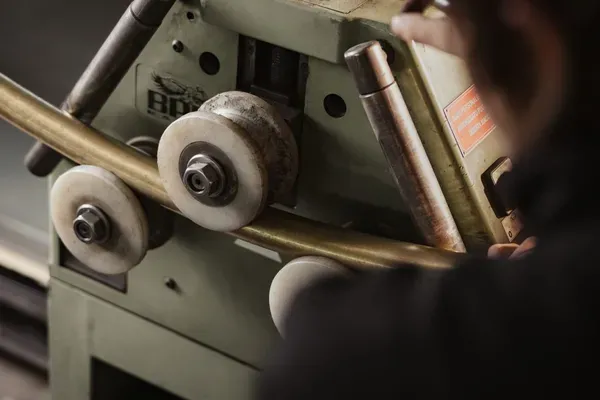 Nahaufnahme einer Metallbearbeitungsmaschine in einer südtiroler Werkstatt; eine Person bedient das Gerät, im Hintergrund Regale mit Werkzeugen.