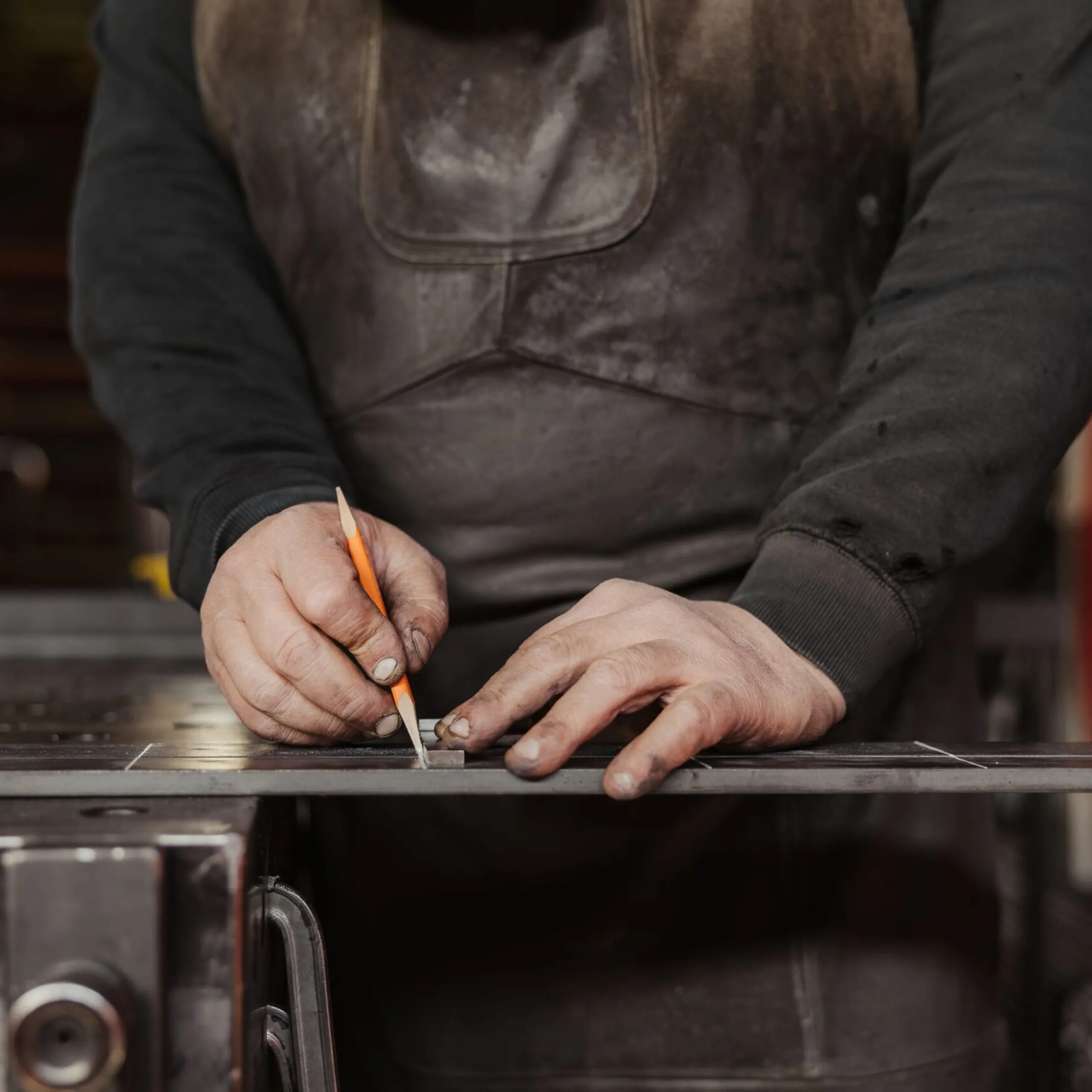Person markiert Metallblech mit Bleistift auf einer Werkbank in einem Metallbaubetrieb in Südtirol; Nahaufnahme der Hände.