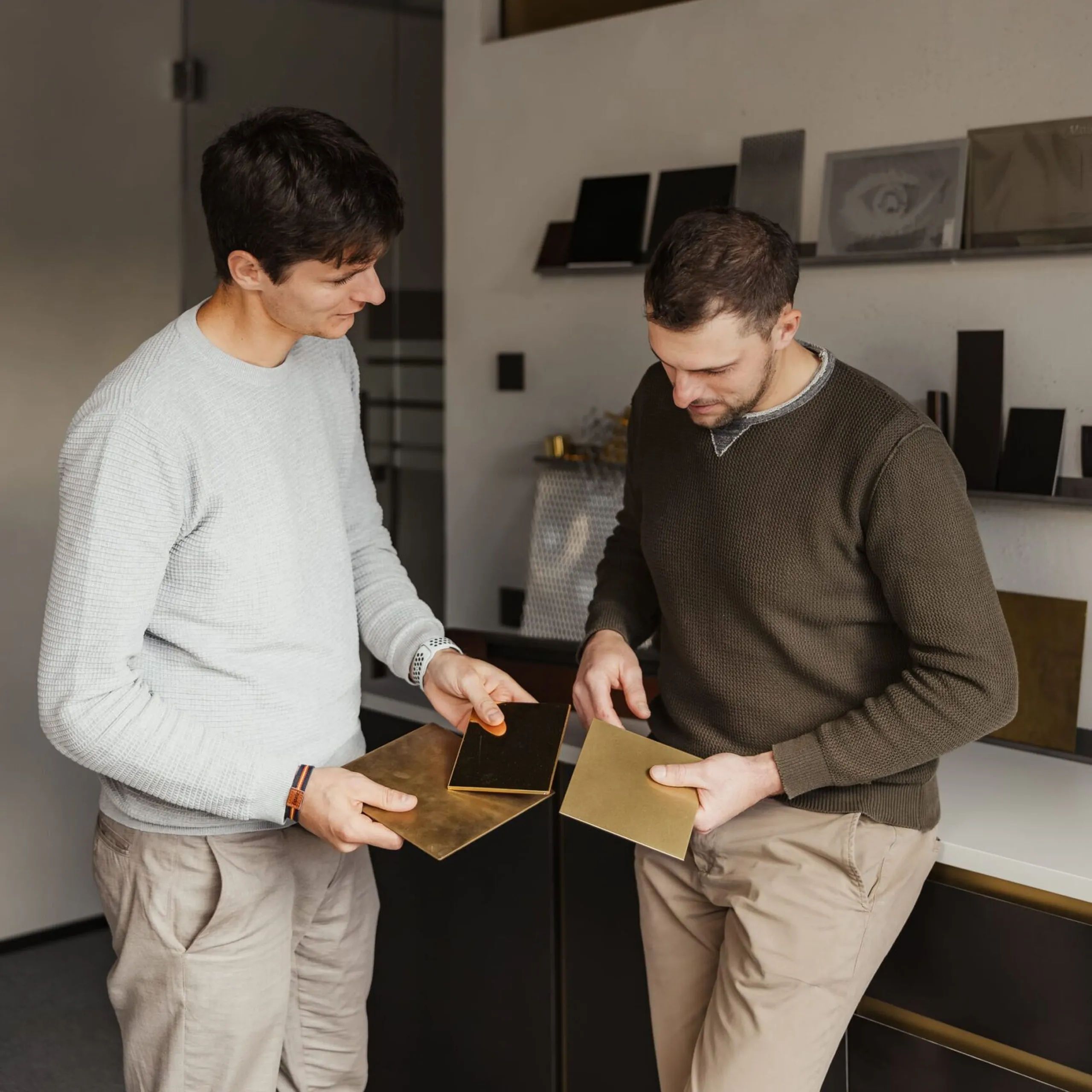 Zwei Mitarbeitende einer Metallbau-Firma in Südtirol prüfen goldene Metallplatten; im Hintergrund Regale mit Musterplatten.
