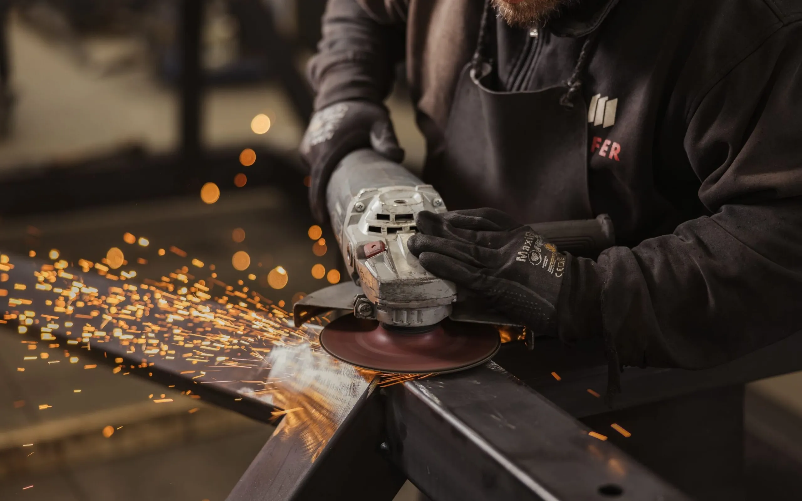 Person in einem Metallbau-Unternehmen in Südtirol schleift einen Metallträger mit einem Winkelschleifer; Funken sprühen.