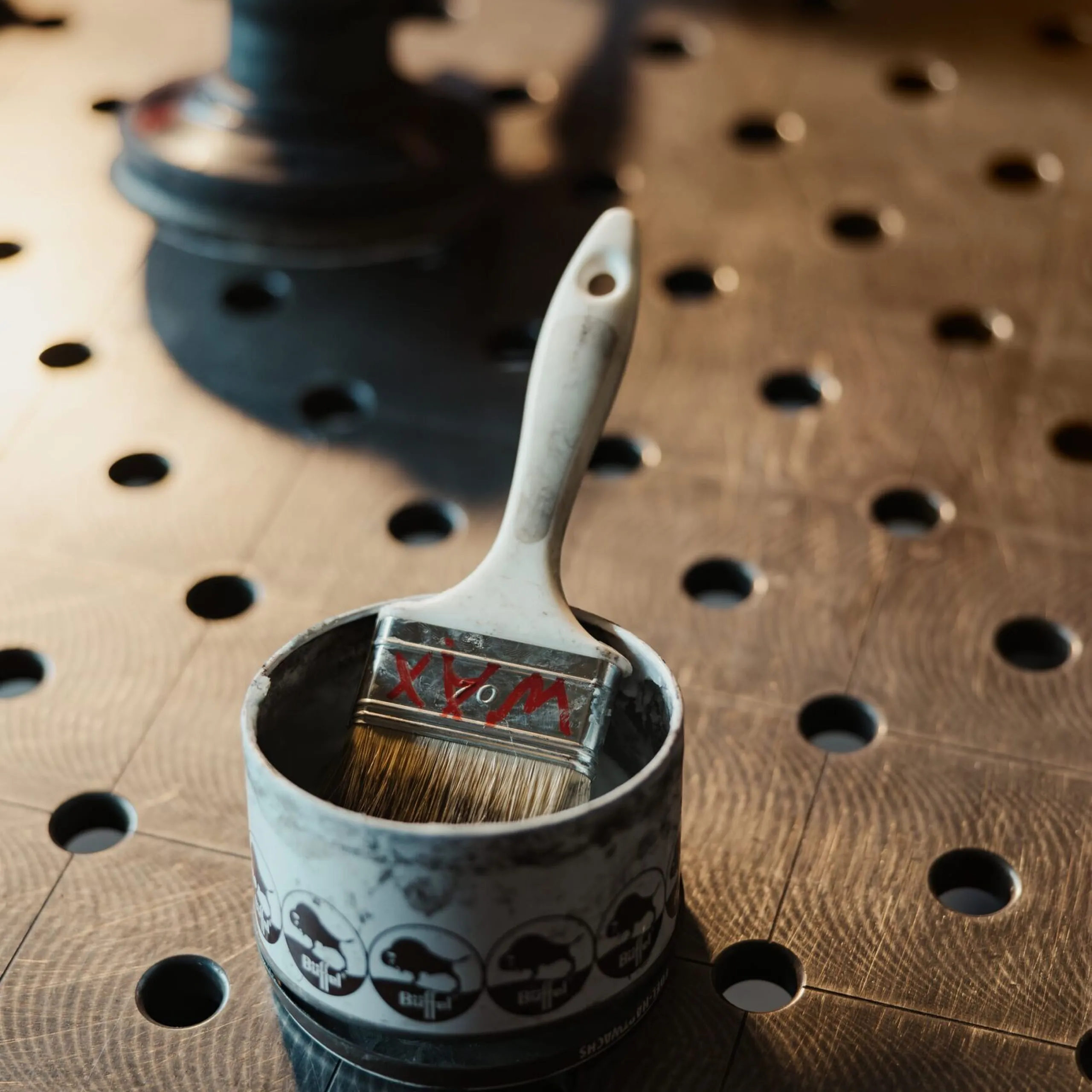 Nahaufnahme eines Metallbehälters mit Pinsel darin auf einer gelochten Metall-Arbeitsfläche; Band mit Schädel-Motiven um den Behälter.