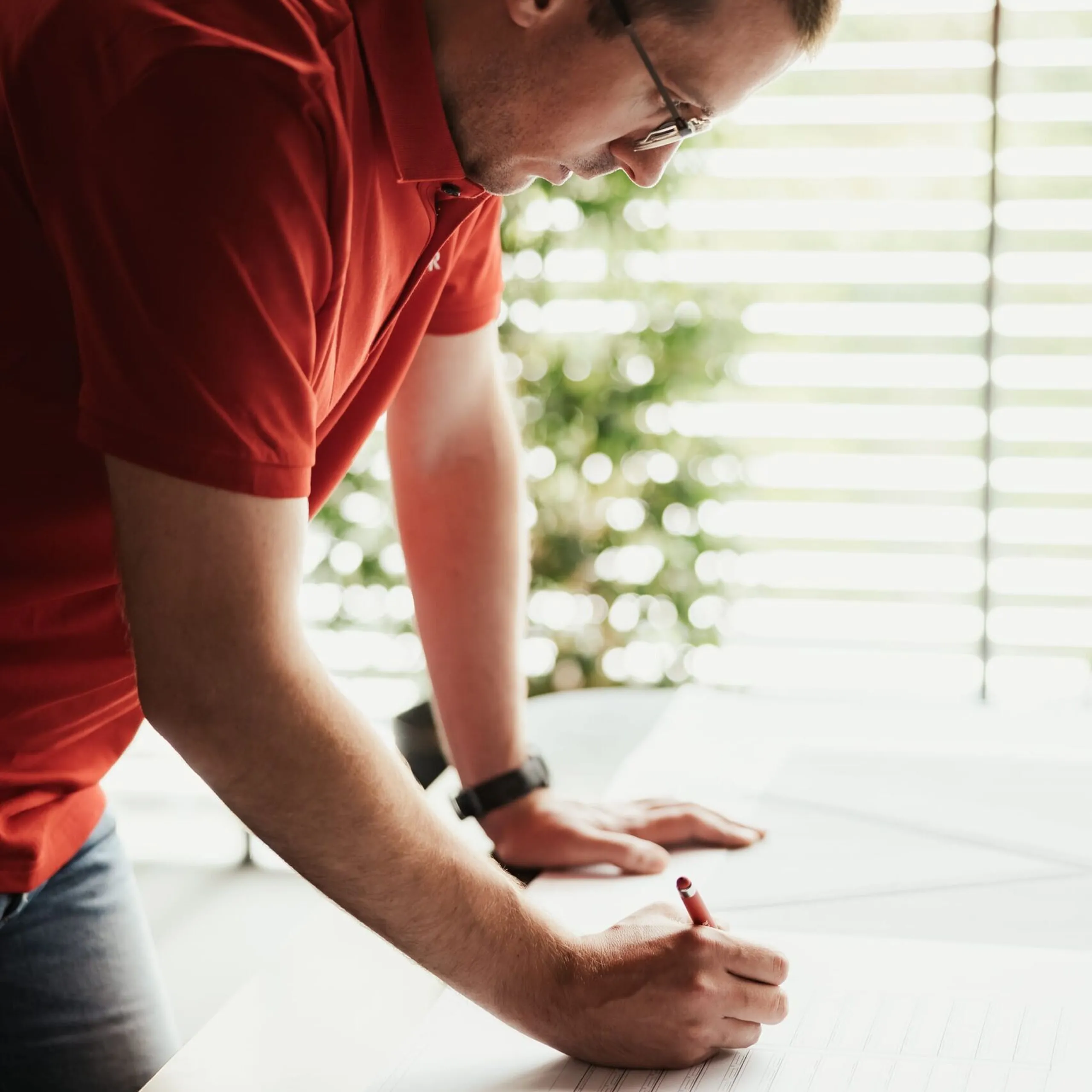 Mitarbeiter eines Metallbauunternehmens aus Südtirol beugt sich über den Tisch und skizziert Konstruktionspläne auf einem großen Papierbogen.