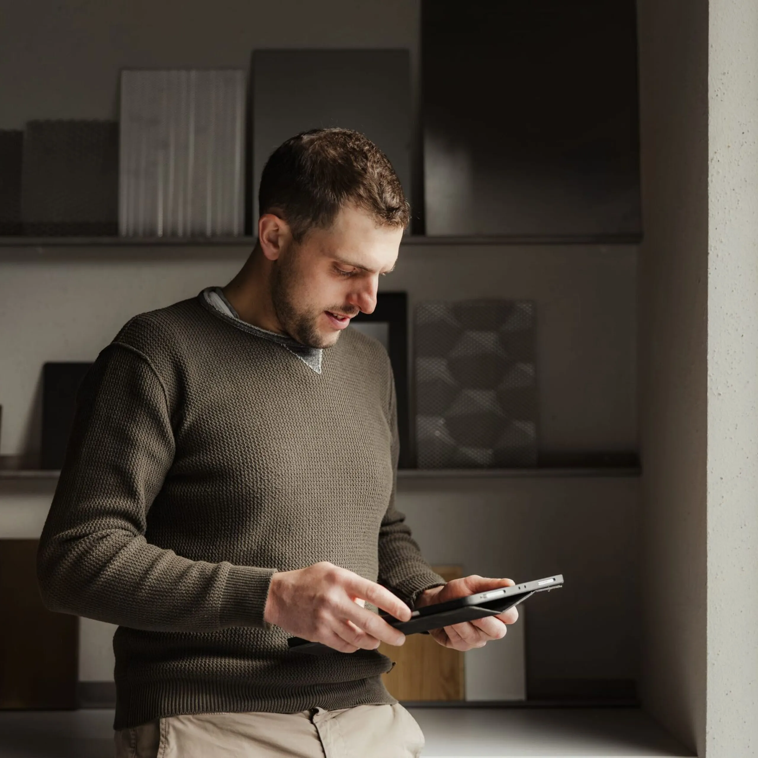 Eine Person steht in einem Innenraum eines Metallbauunternehmens in Südtirol und betrachtet ein Tablet; im Hintergrund Metallproben und Muster.