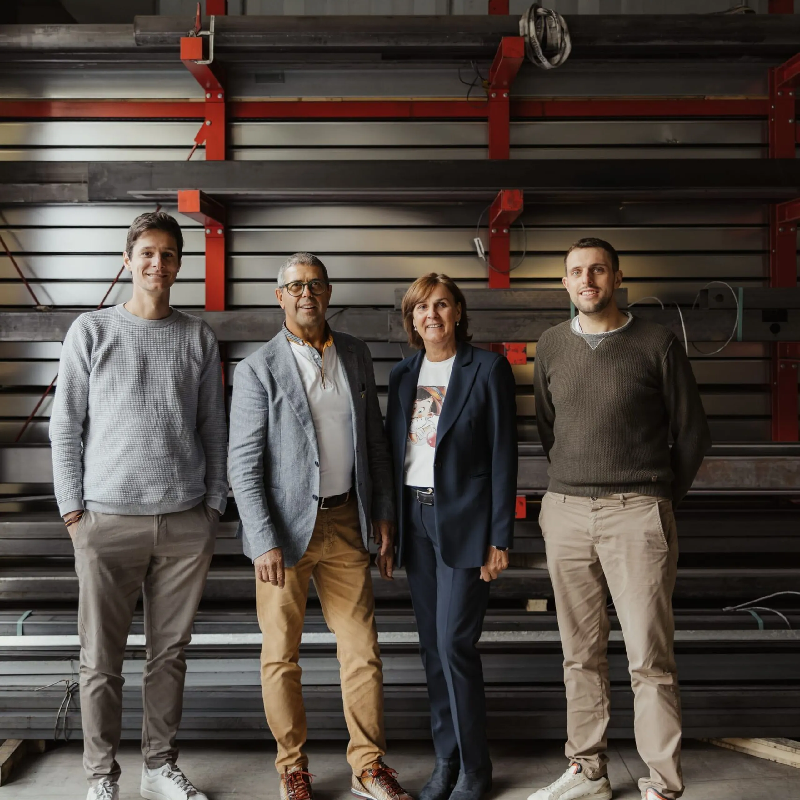Vier Mitarbeitende eines Metallbauunternehmens aus Südtirol stehen vor Stahlregalen in einer Werkstatt, lächeln in die Kamera.