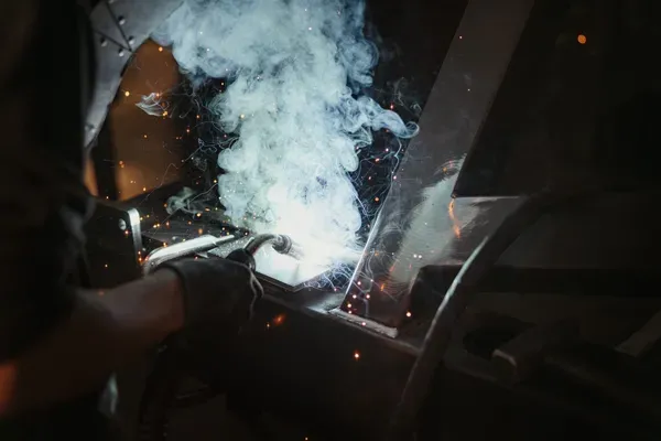 Eine Person schweißt an einer Metallkonstruktion in einem Südtiroler Betrieb; Funken und Rauch umgeben den Lichtbogen.