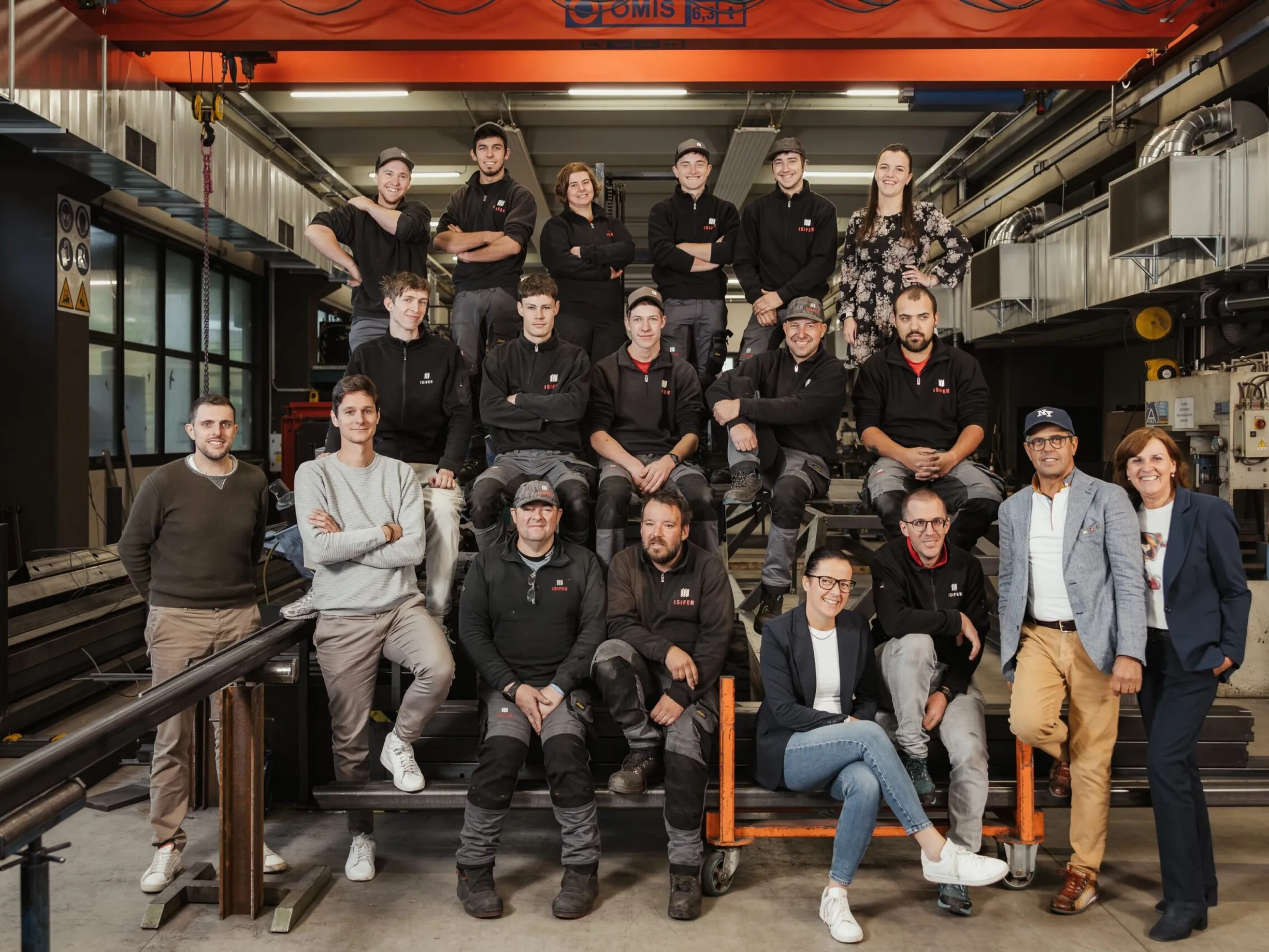 Gruppenporträt eines Metallbau-Teams in einer Südtiroler Werkstatt, vor Maschinen und einem Hallenkran.