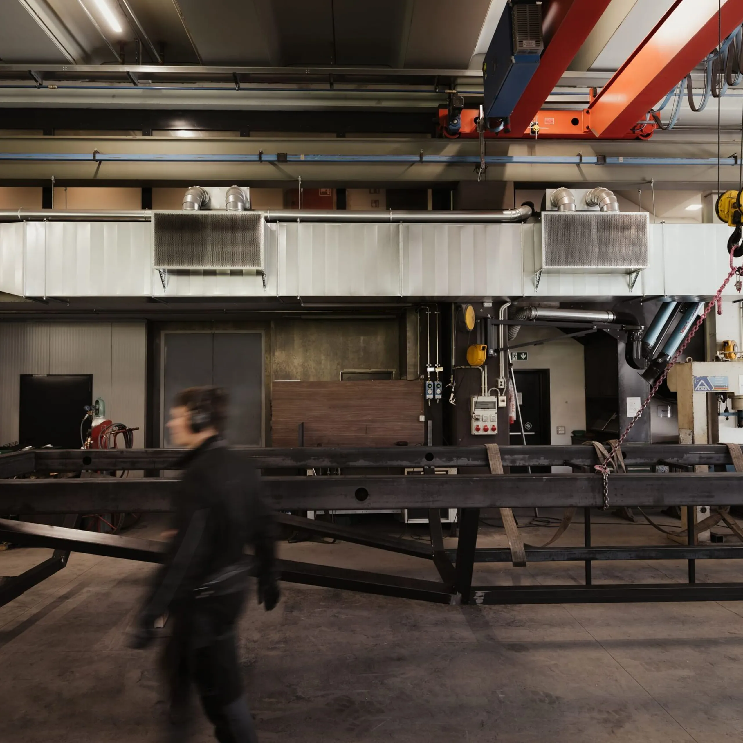 Industriehalle in Südtirol mit schweren Stahlträgern, Oberkran, Lüftungskanälen und Werkstattausstattung; eine Person läuft vorbei.
