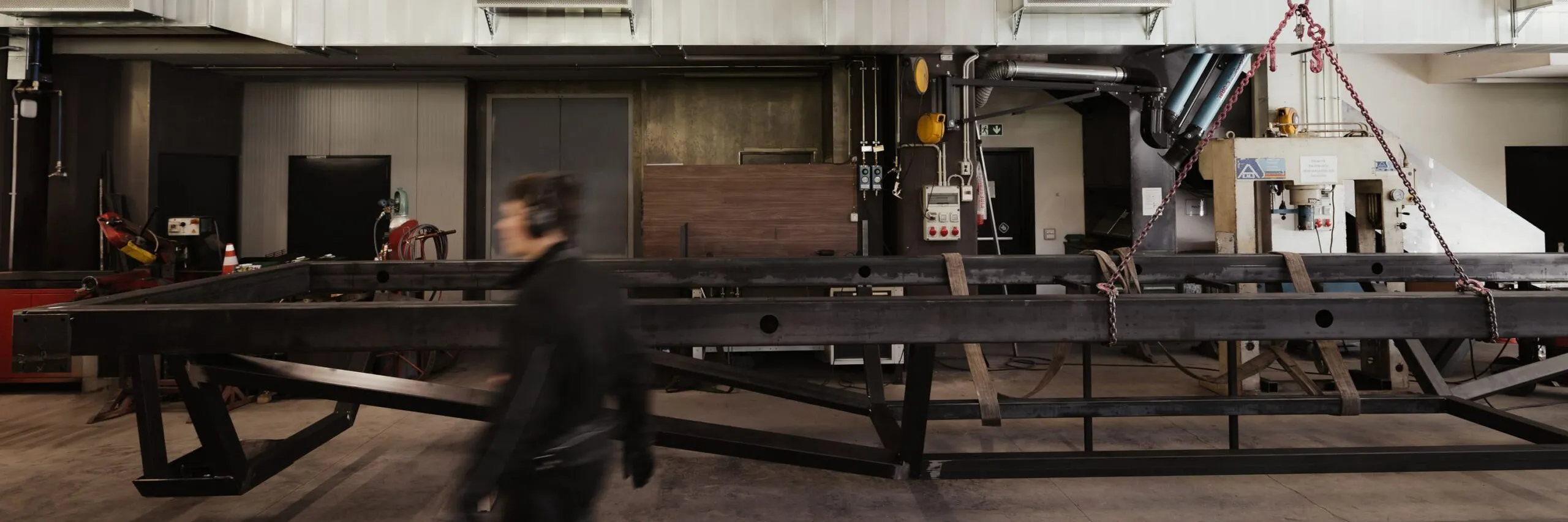 Industriehalle in Südtirol mit schweren Stahlträgern, Oberkran, Lüftungskanälen und Werkstattausstattung; eine Person läuft vorbei.