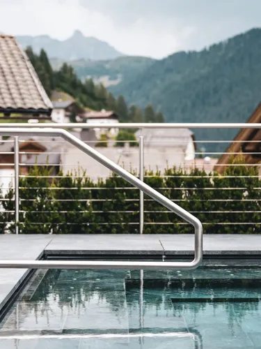 Moderne Edelstahlgeländer um einen Dachpool; Blick auf Berge und Südtiroler Häuser mit Ziegeldächern im Hintergrund.