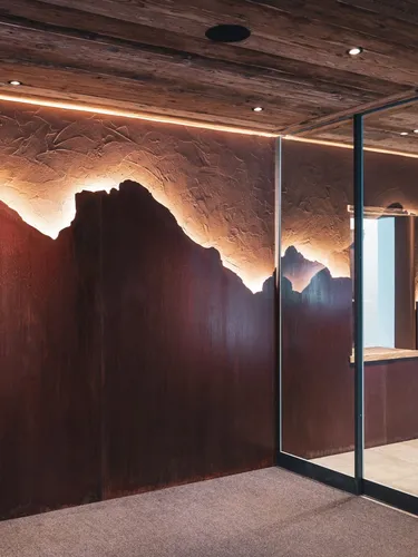 Innenraum eines Metallbau-Unternehmens in Südtirol: beleuchtete Kupferberg-Silhouette an Holzwand, Glaswand mit Metallrahmen, Skulptur im Hintergrund.
