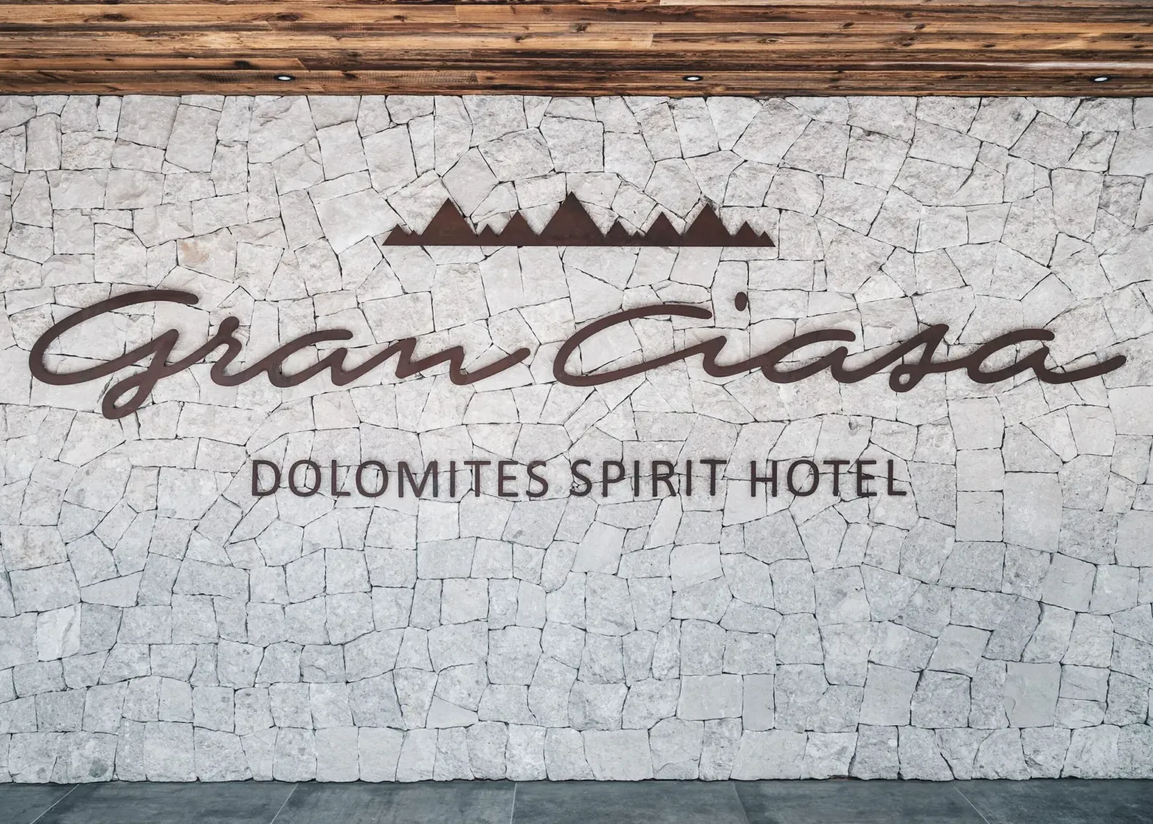 Steinwand mit dunkelbraunem, kursivem Schriftzug und Bergsilhouette; darunter Dolomites Spirit Hotel.