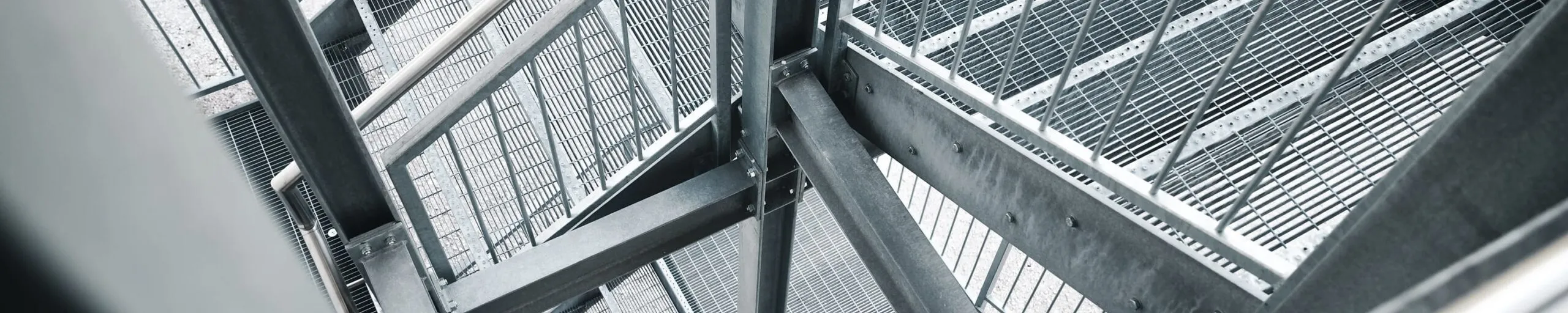 Mehrstöckige Außentreppe aus Stahl mit Geländern und Gitterstufen; verschachteltes Metallgerüst, diagonale Perspektive durch die Metallkonstruktion.