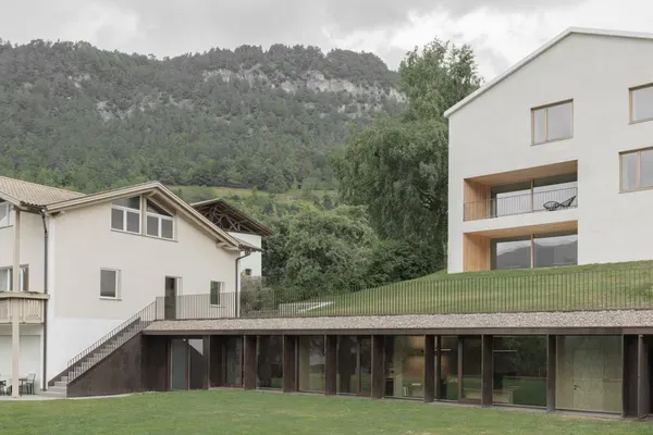 Complesso aziendale moderno in Alto Adige: edifici bianchi con grandi finestre, terrazze in legno e piano terra vetrato su prato verde.