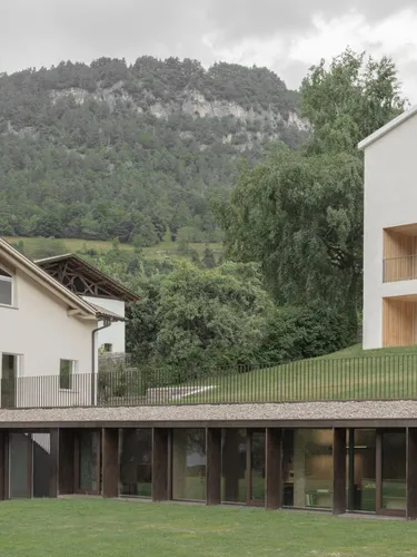 Complesso aziendale moderno in Alto Adige: edifici bianchi con grandi finestre, terrazze in legno e piano terra vetrato su prato verde.
