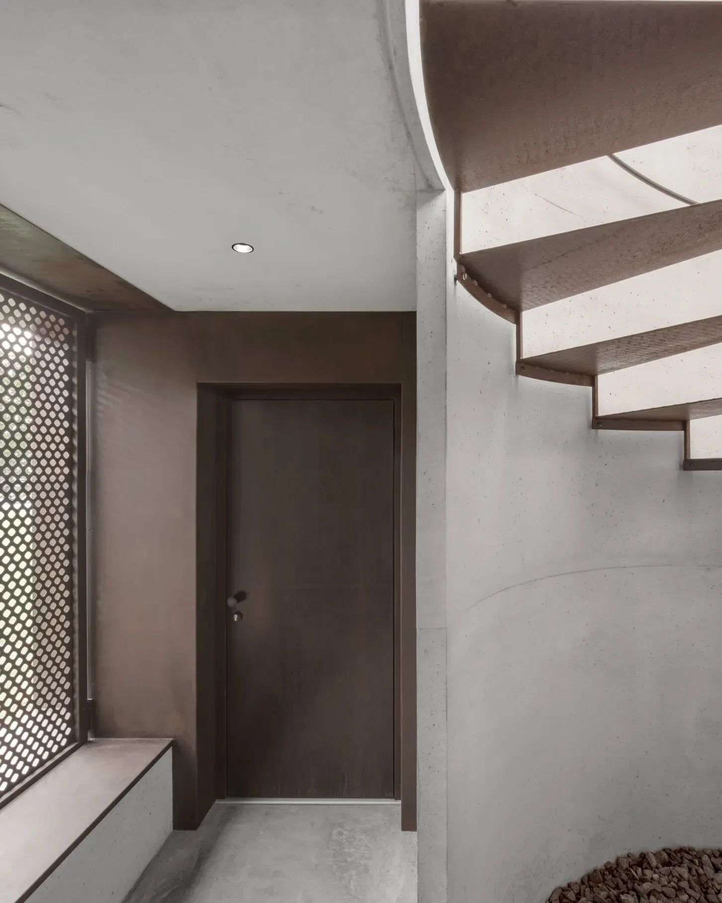 Ingresso industriale: porta marrone, scala metallica a destra, pareti in cemento e pannello forato a sinistra.