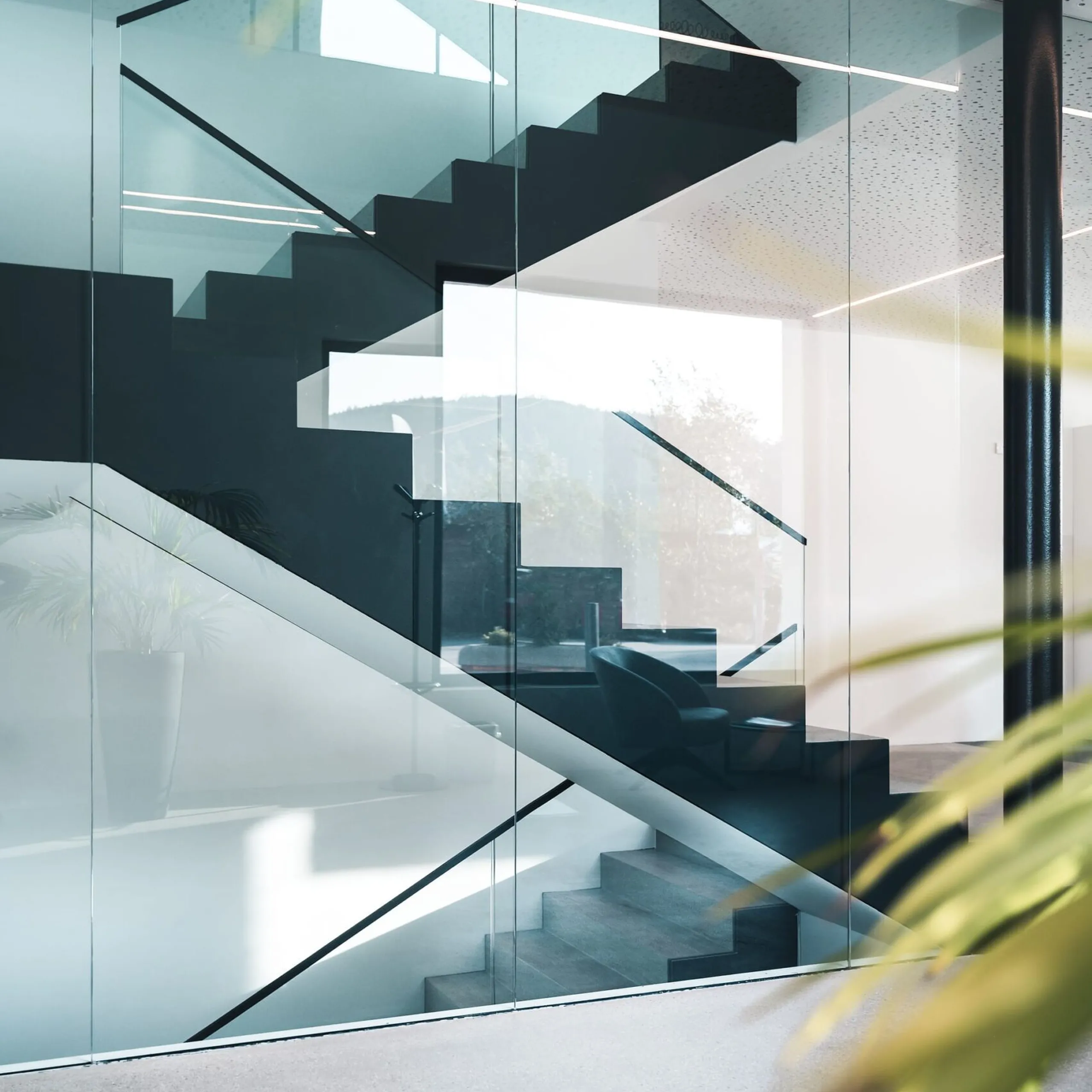 Moderne Innenansicht einer Glas- und Stahltreppe hinter Glaswänden, klare Linien, Lichtstreifen und Spiegelungen in einer Metallbaufirma in Südtirol.