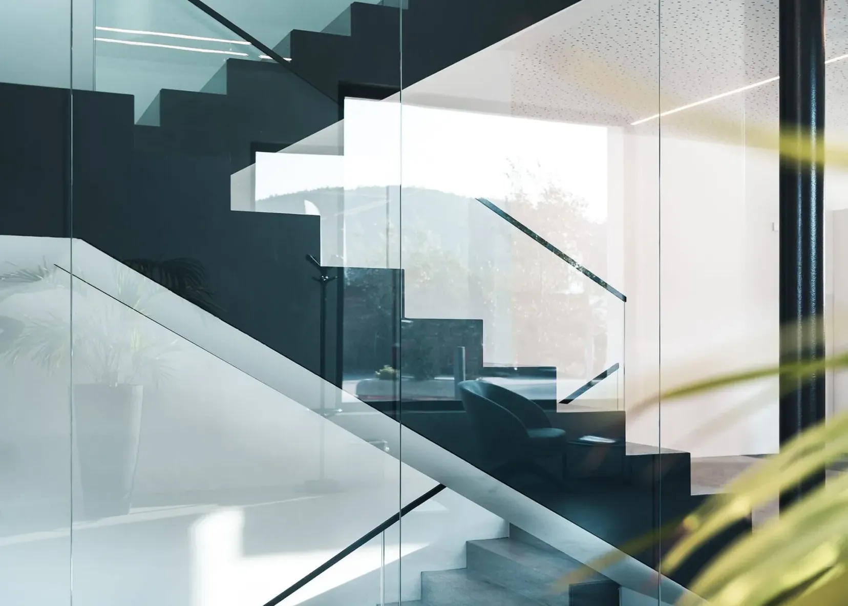 Moderne Innenansicht einer Glas- und Stahltreppe hinter Glaswänden, klare Linien, Lichtstreifen und Spiegelungen in einer Metallbaufirma in Südtirol.