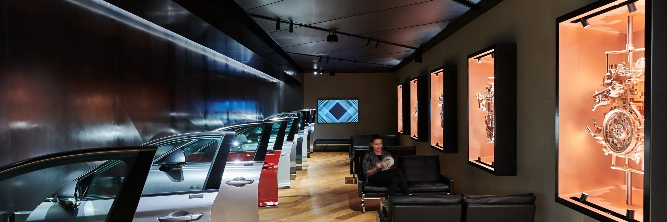 Ausstellungsraum eines Metallbau-Unternehmens in Südtirol: links Autotüren, rechts Motorexponate; eine Person sitzt auf schwarzem Ledersofa.