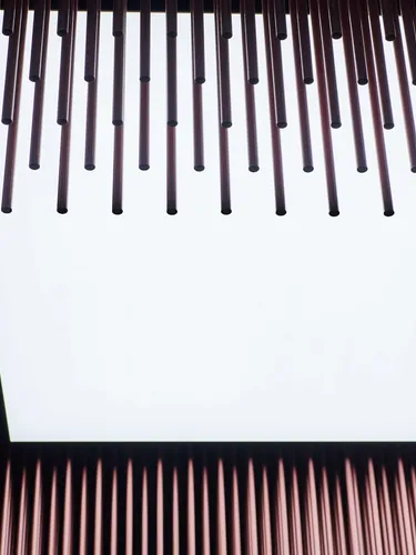 Blick von unten auf eine Deckeninstallation aus vielen kupferfarbigen Metallstangen, die eine helle quadratische Lichtöffnung einrahmen.