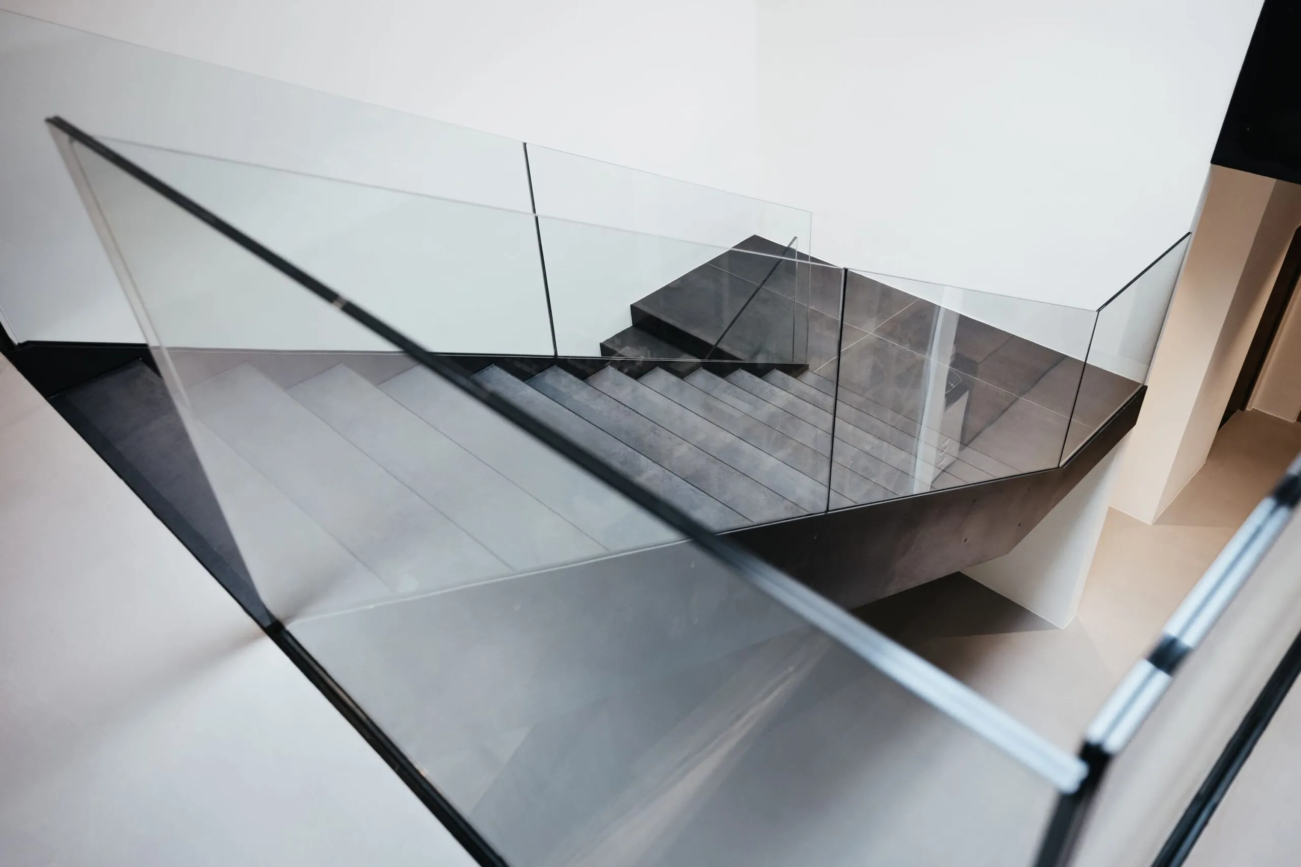 Moderne Metalltreppe mit Glasgeländer, aus schräger Perspektive aufgenommen; heller Innenraum mit reflektierenden Glas- und Stahlflächen.