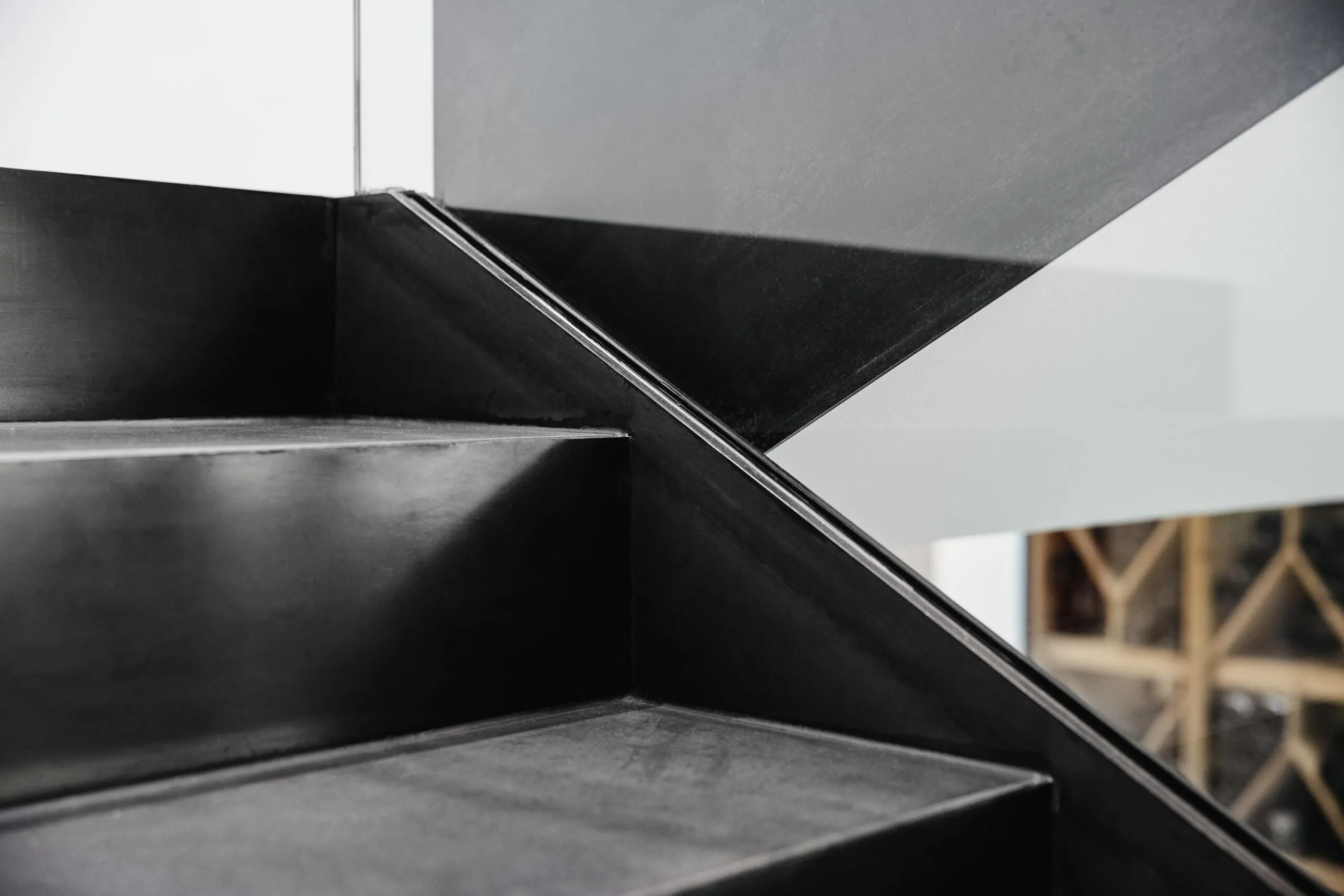 Nahaufnahme einer schwarzen Metalltreppe mit diagonalem Stützprofil, grauer Hintergrund.