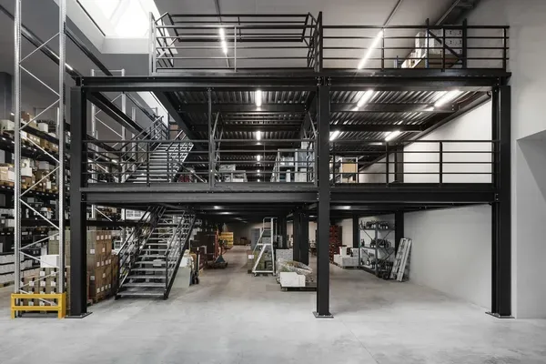 Große Lagerhalle mit schwarzer Stahlkonstruktion, Zwischenebene, Treppen, Geländer, Regale und Paletten – Stahlbau in Südtirol.