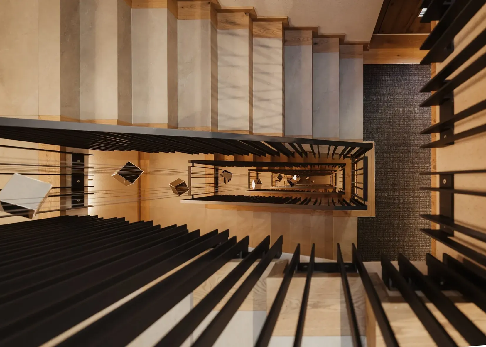 Vista dall'alto di una scala interna con parapetti neri e gradini in legno chiaro, un pozzo verticale che forma motivi geometrici verso il basso.