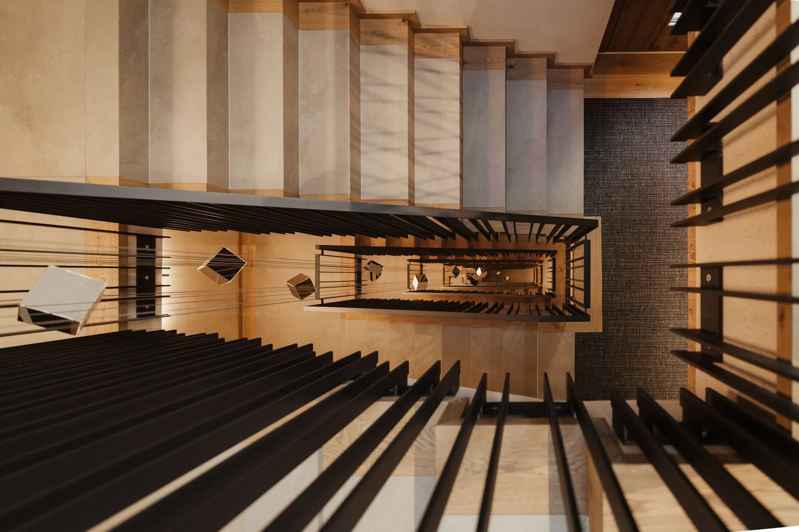 Vista dall'alto di una scala interna con parapetti neri e gradini in legno chiaro, un pozzo verticale che forma motivi geometrici verso il basso.