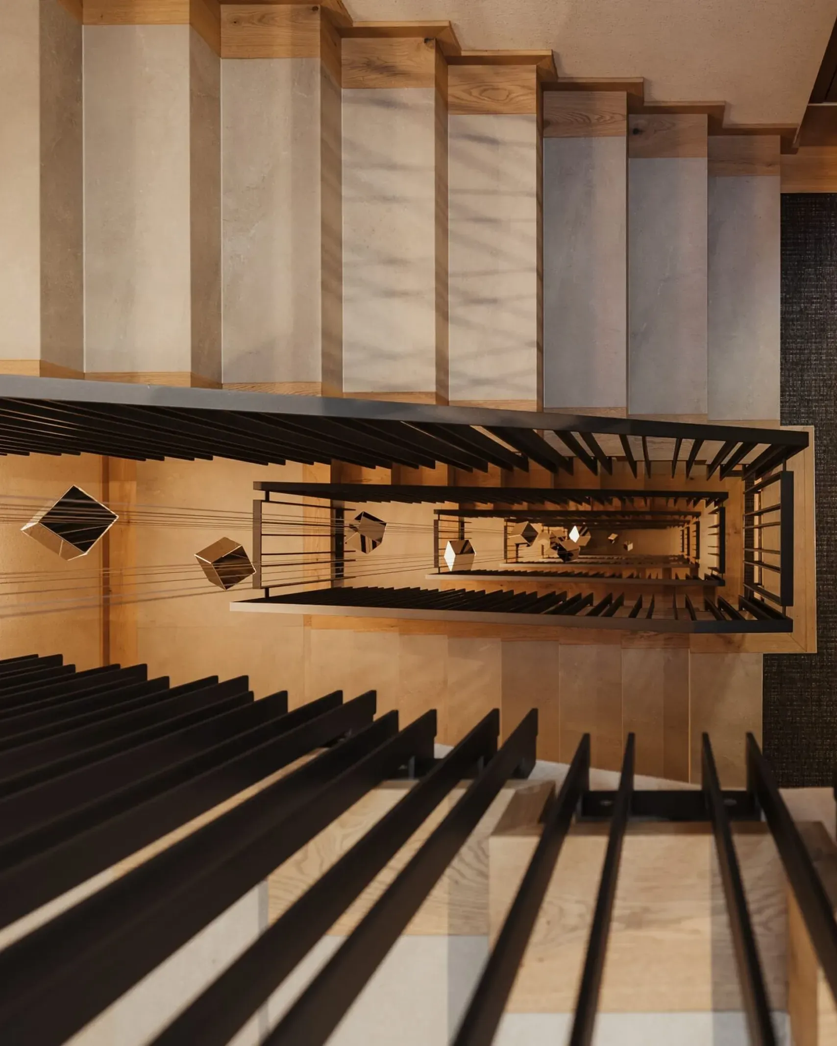Vista dall'alto di una scala interna con parapetti neri e gradini in legno chiaro, un pozzo verticale che forma motivi geometrici verso il basso.