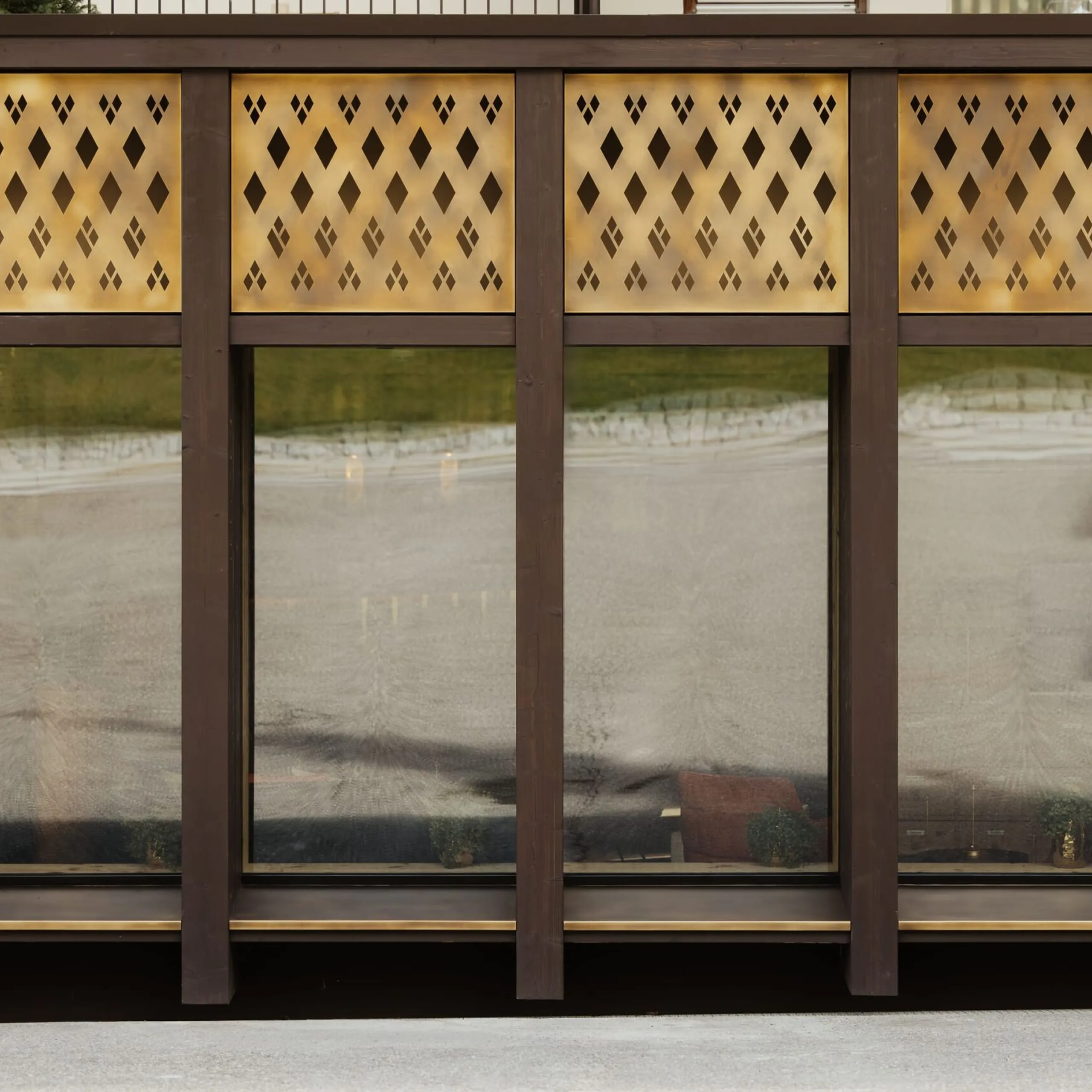 Fassade eines Metallbau-Unternehmens in Südtirol: dunkle Stützen, goldene Lochbleche über großen Fenstern, reflektierende Glasfront.