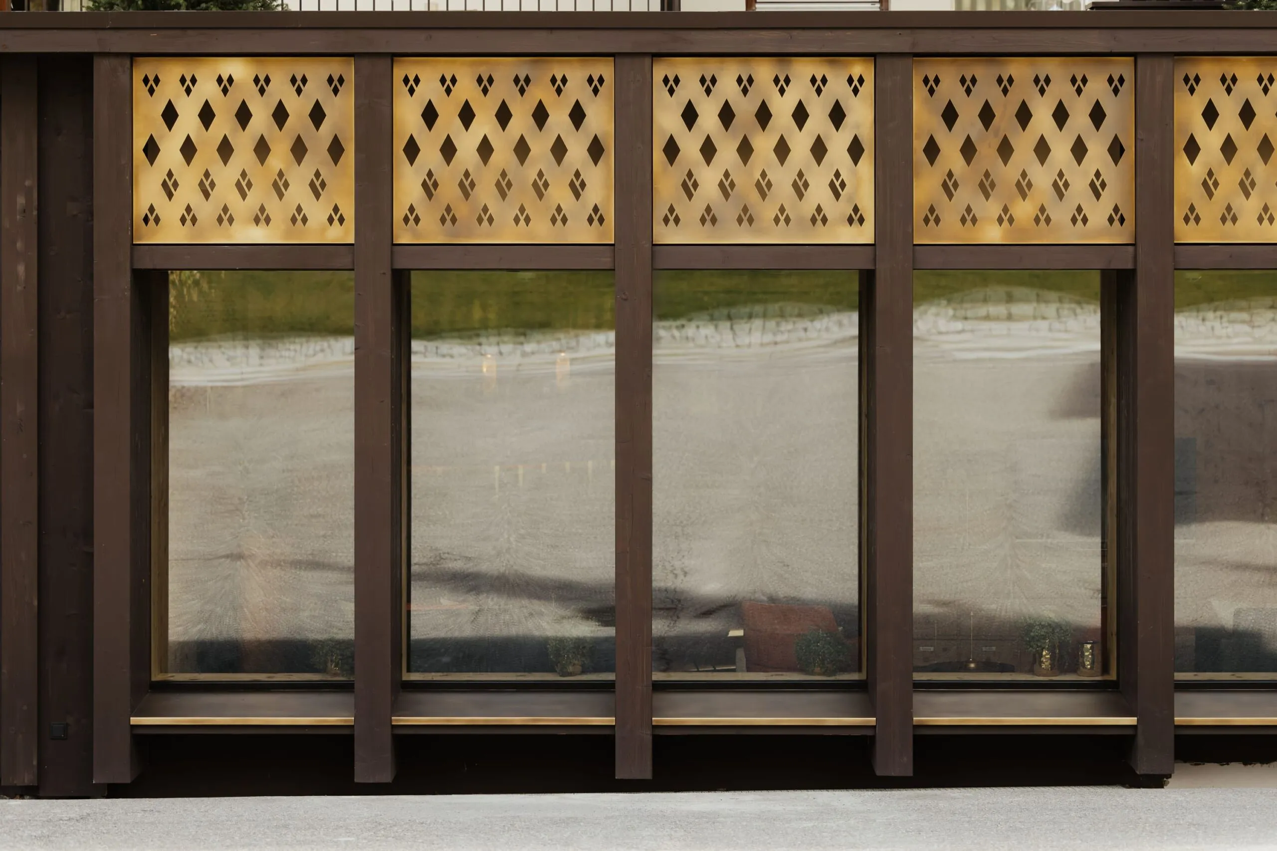 Fassade eines Metallbau-Unternehmens in Südtirol: dunkle Stützen, goldene Lochbleche über großen Fenstern, reflektierende Glasfront.