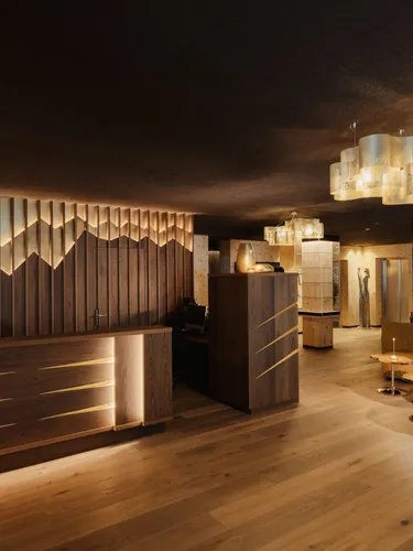 Empfangs- und Loungebereich eines Metallbau-Unternehmens in Südtirol: warme Holzmöbel, dunkle Wandverkleidung, stilvolle Leuchten, Bar und beige-goldene Couch.