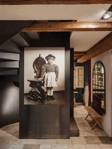 Interno di azienda metalmeccanica: scala a chiocciola nera su pannello nero, foto d'epoca di una bambina, travi in legno, tenda rossa e finestra ad arco.