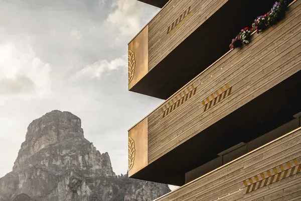 Edificio in legno a più piani con frecce gialle di segnalazione sui bordi, balconi sporgenti e fioriere, con una montagna rocciosa sullo sfondo.