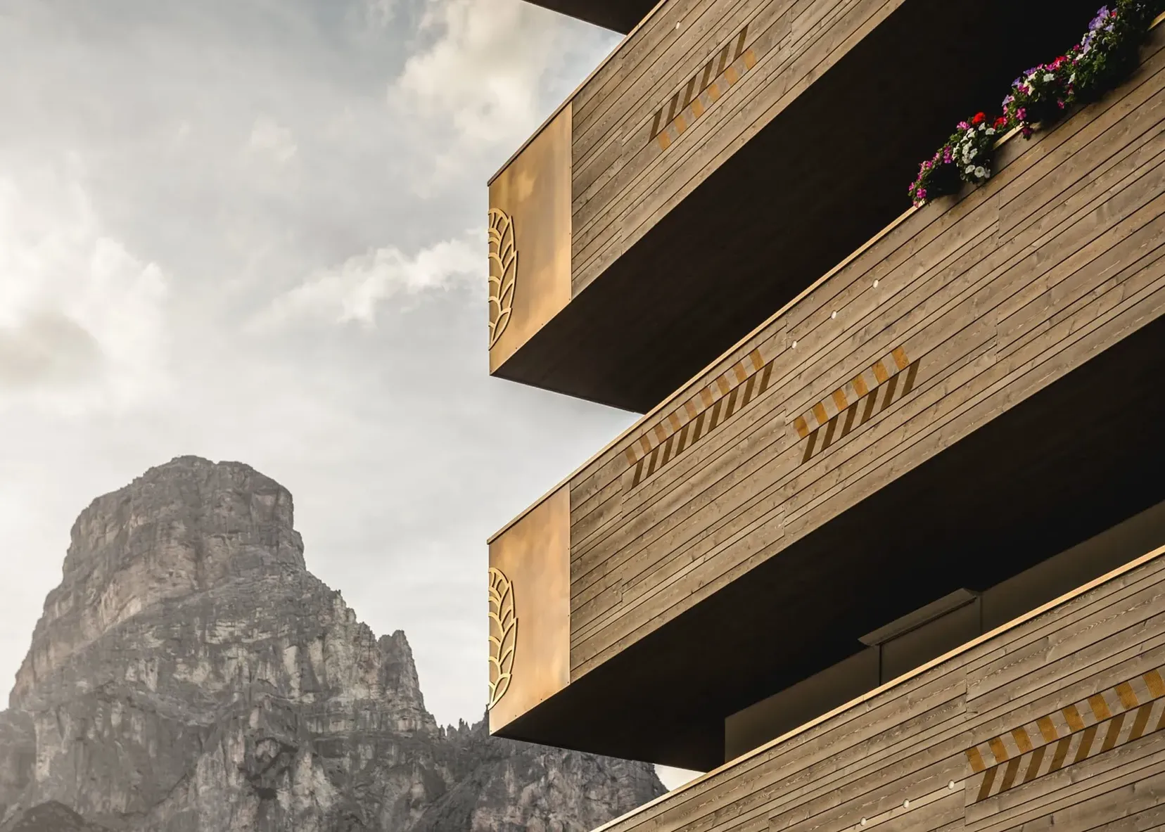 Edificio in legno a più piani con frecce gialle di segnalazione sui bordi, balconi sporgenti e fioriere, con una montagna rocciosa sullo sfondo.