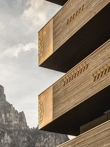 Edificio in legno a più piani con frecce gialle di segnalazione sui bordi, balconi sporgenti e fioriere, con una montagna rocciosa sullo sfondo.