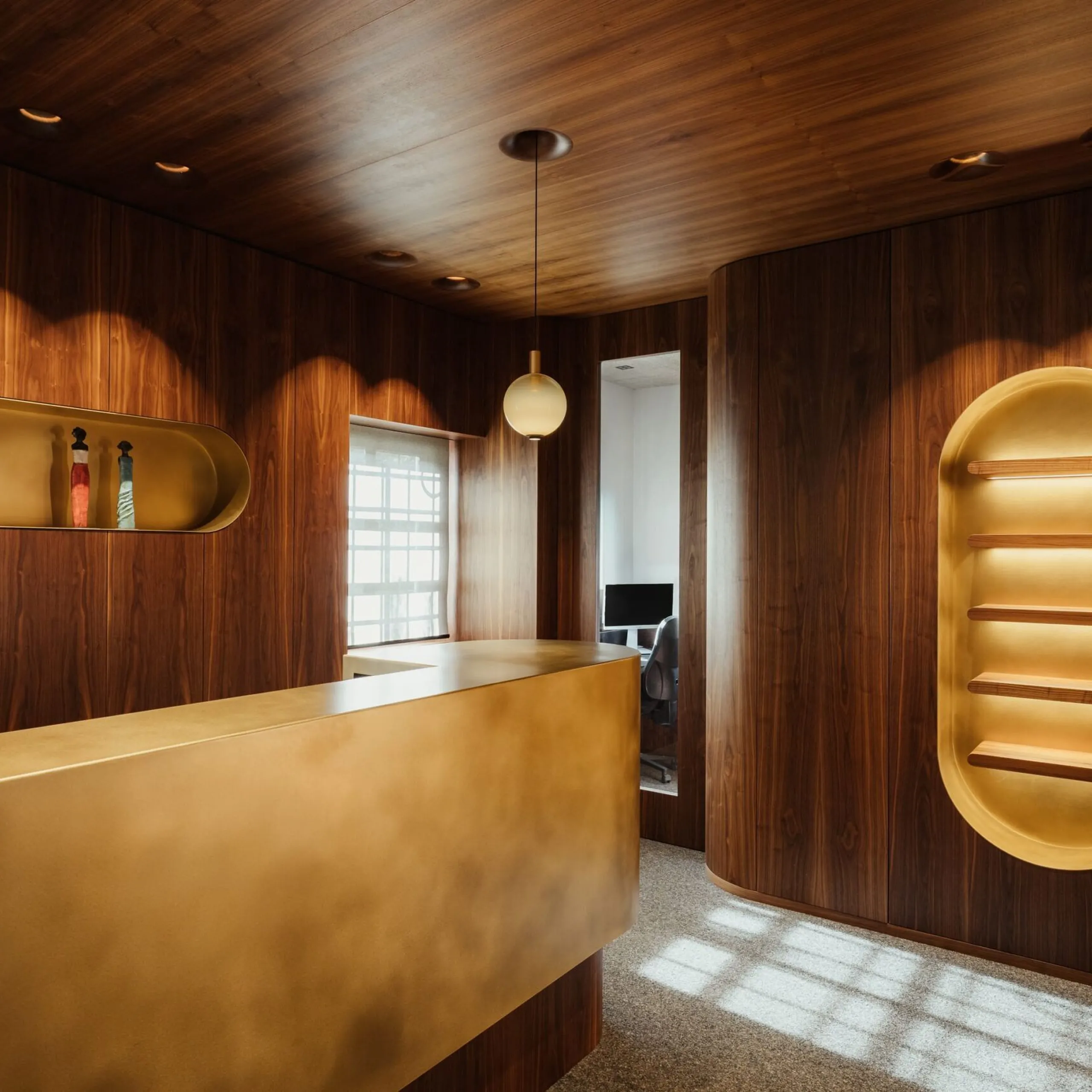 Interno di un'azienda metalmeccanica in Alto Adige: pareti e soffitto in legno scuro, reception dorata, nicchie illuminate e zona lavoro con computer.