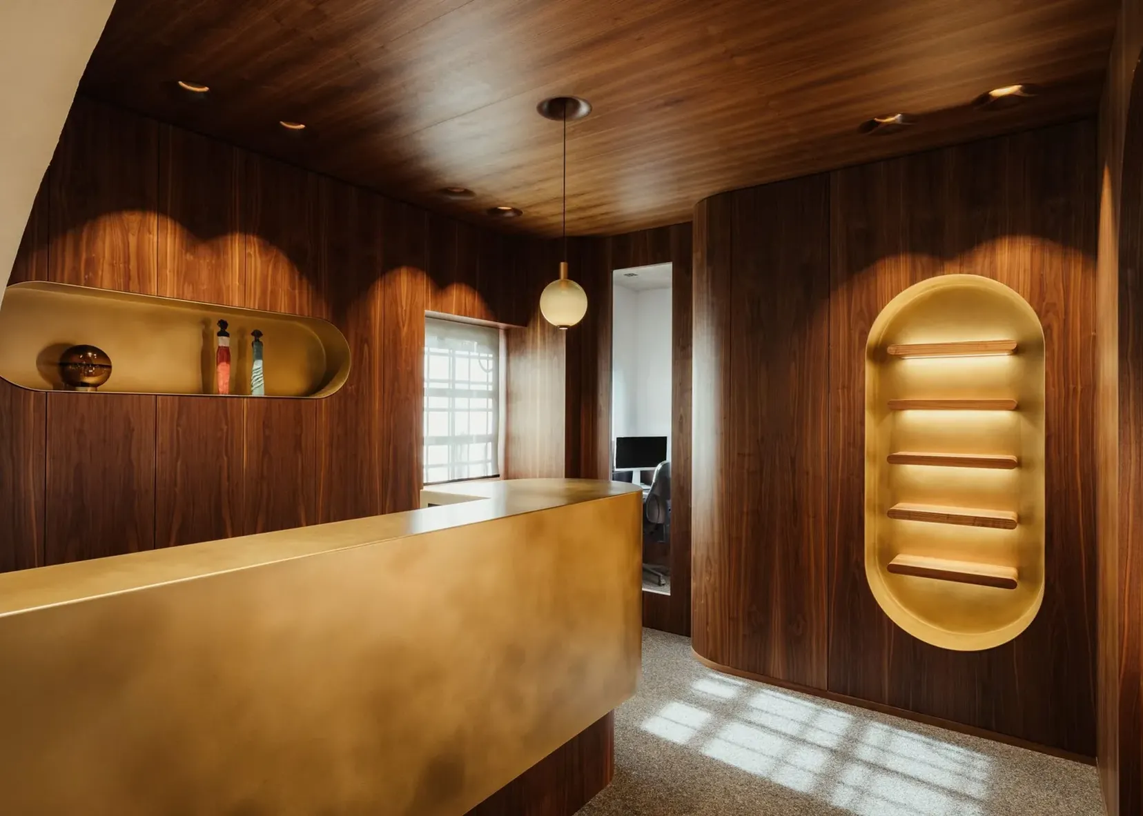 Interno di un'azienda metalmeccanica in Alto Adige: pareti e soffitto in legno scuro, reception dorata, nicchie illuminate e zona lavoro con computer.