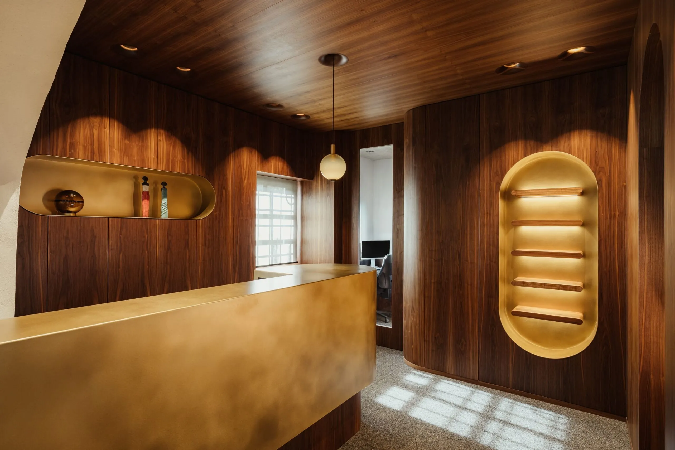 Interno di un'azienda metalmeccanica in Alto Adige: pareti e soffitto in legno scuro, reception dorata, nicchie illuminate e zona lavoro con computer.