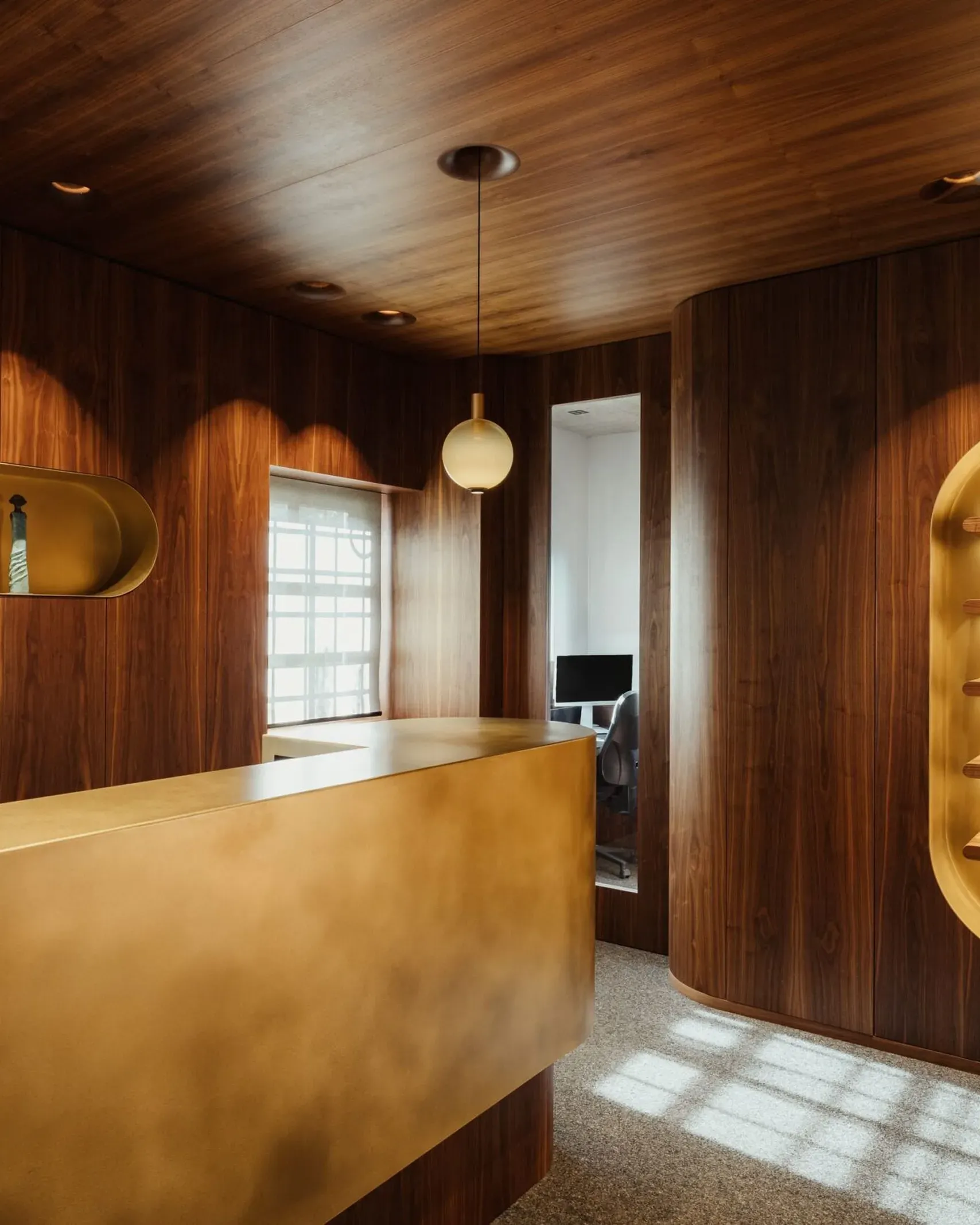 Interno di un'azienda metalmeccanica in Alto Adige: pareti e soffitto in legno scuro, reception dorata, nicchie illuminate e zona lavoro con computer.