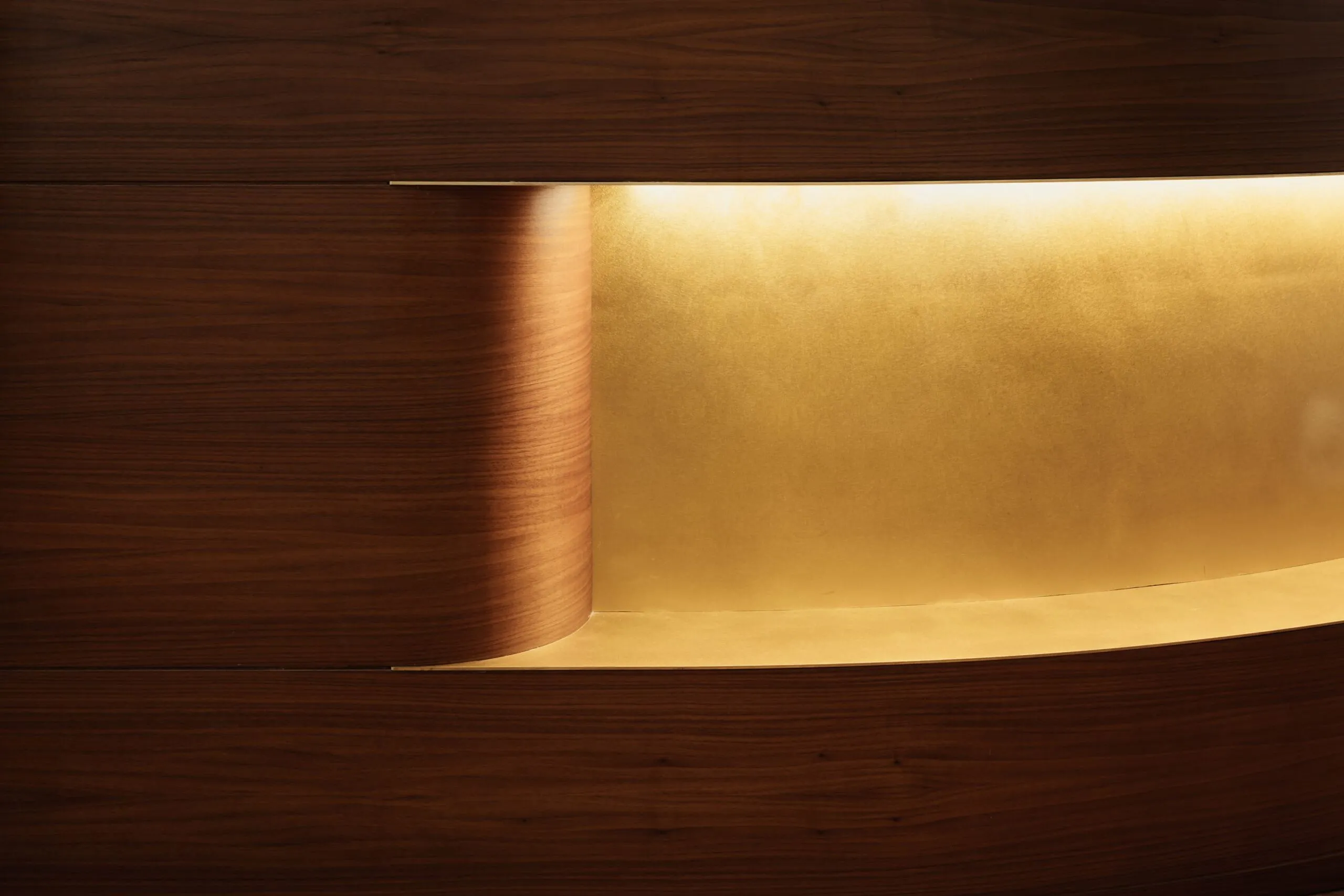 Superficie metallica dorata curvata tra pannelli di legno scuro, illuminata da luce soffusa; interno di azienda metalmeccanica del Sudtirolo.